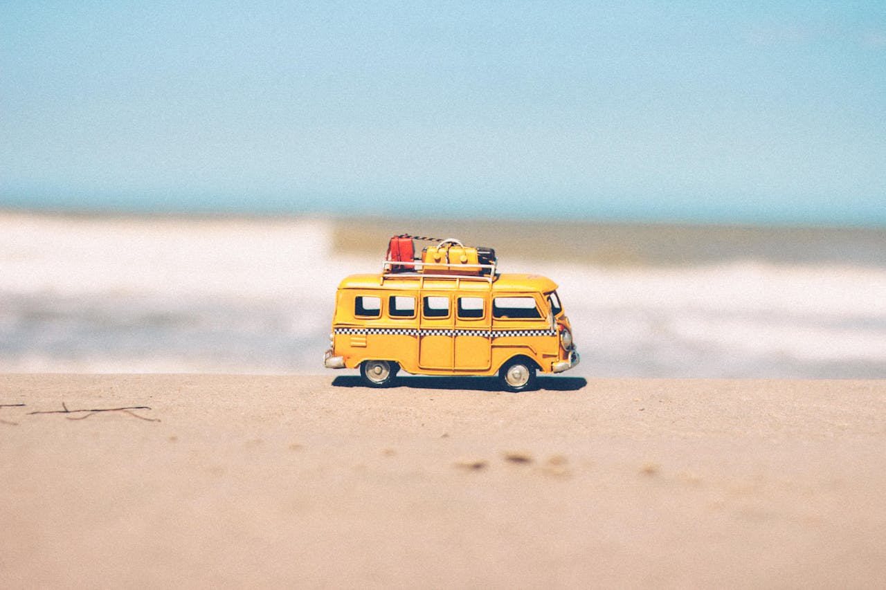 journey A vibrant yellow toy van sits on a sandy beach with an ocean backdrop, symbolizing fun travel adventures.
